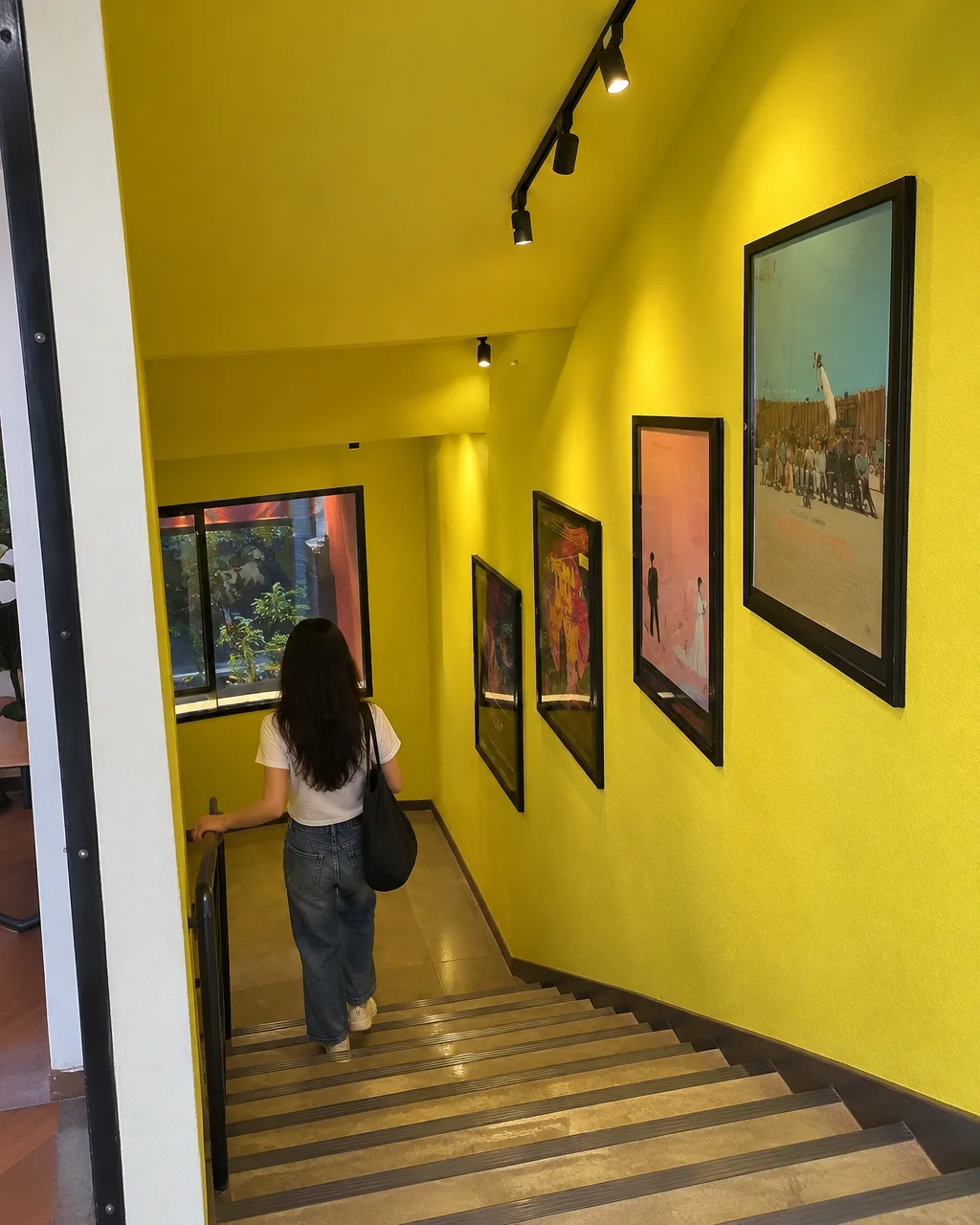 A woman walks down a vibrant yellow stairwell lined with framed art prints along the wall.