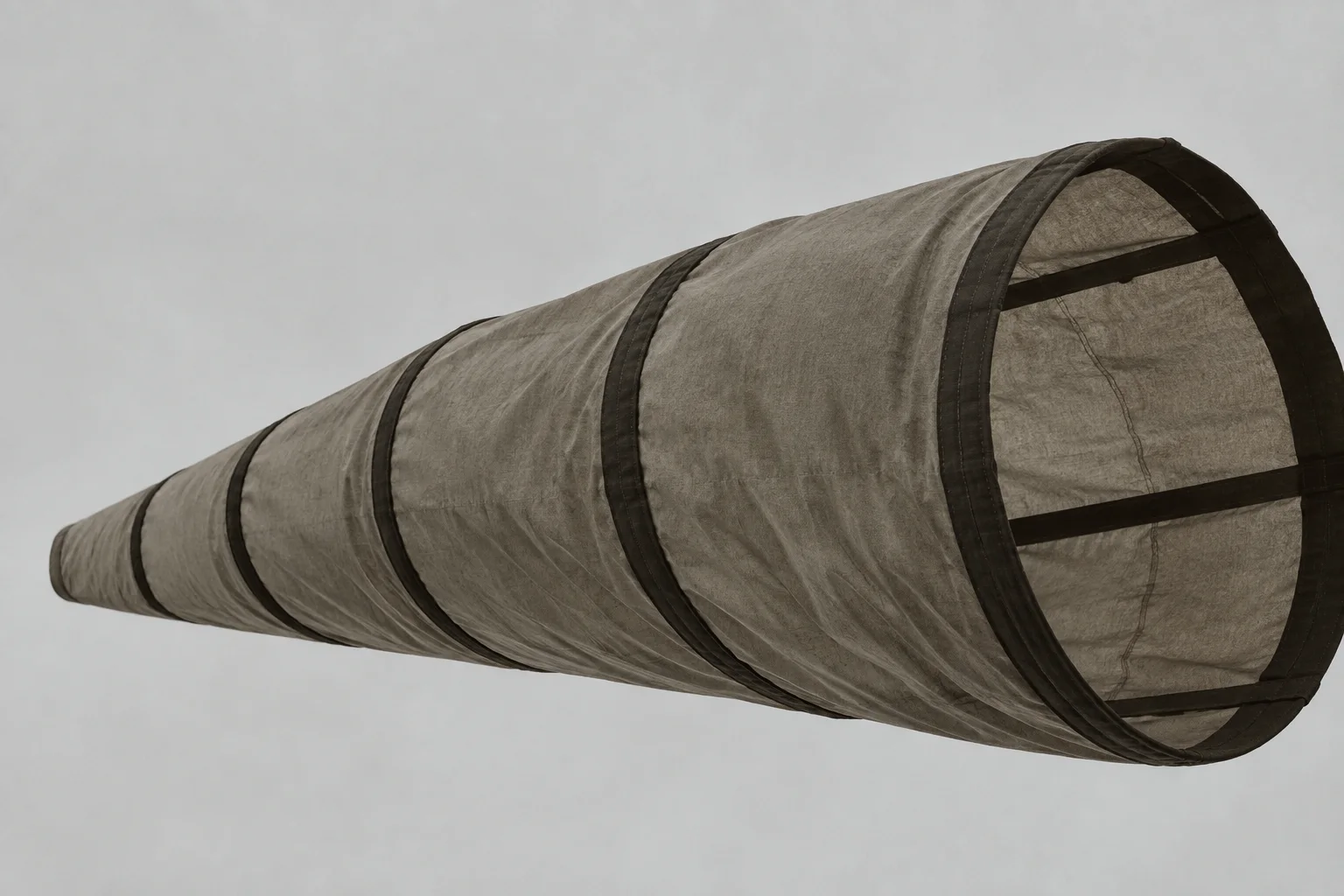 A long fabric windsock with dark reinforcement bands stretches diagonally across a flat, overcast grey sky.
