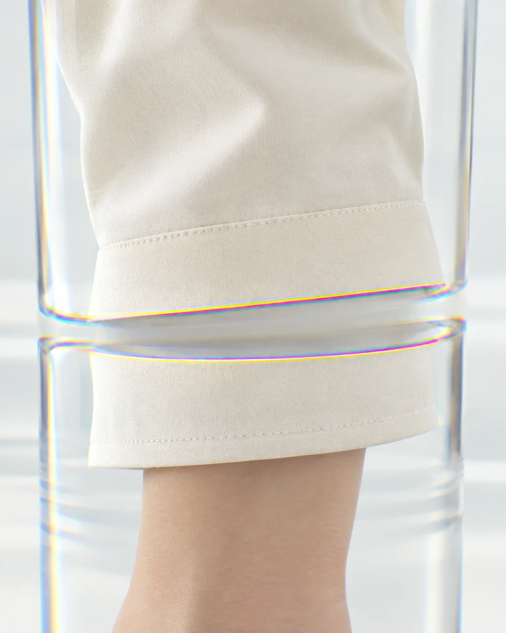 A minimalist cream sleeve cuff seen through a curved glass lens with prismatic chromatic aberration along the edge.