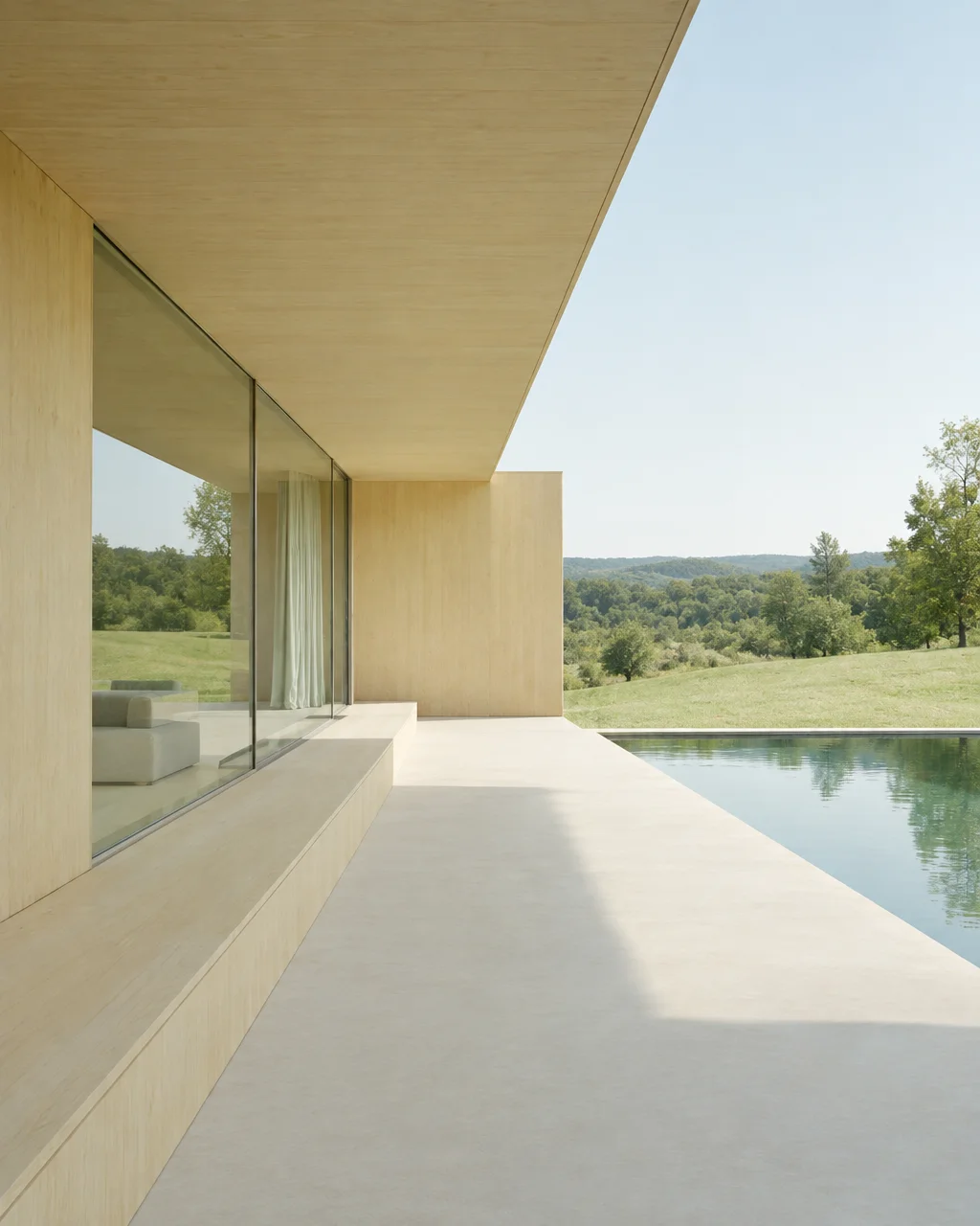 A minimalist modern house terrace with pale wood cladding and glass walls alongside a calm swimming pool overlooking green rolling hills.