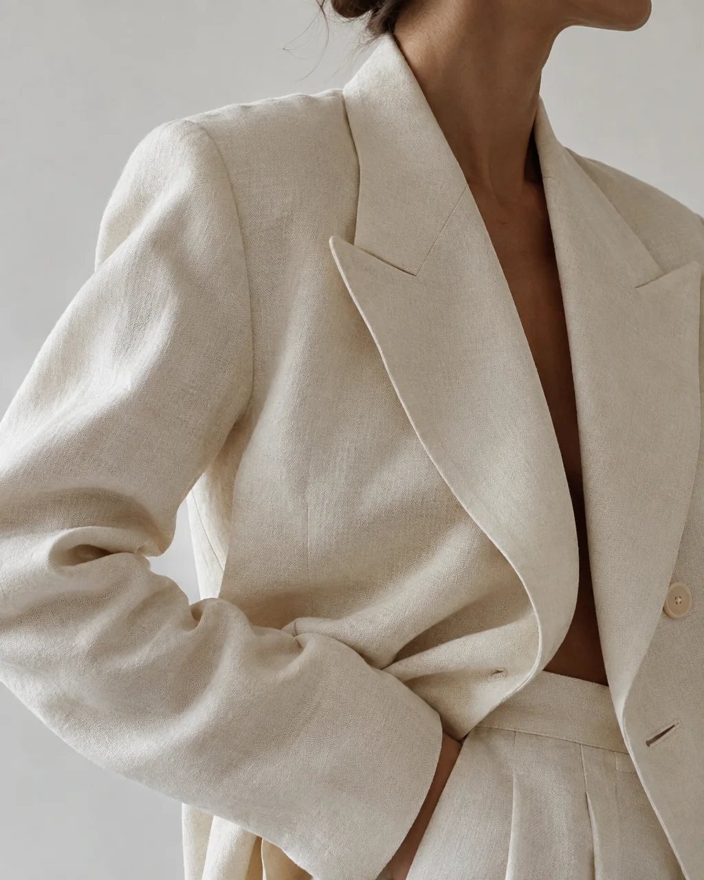 A cropped view of a person wearing an off-white tailored linen suit with wide lapels in soft studio lighting.