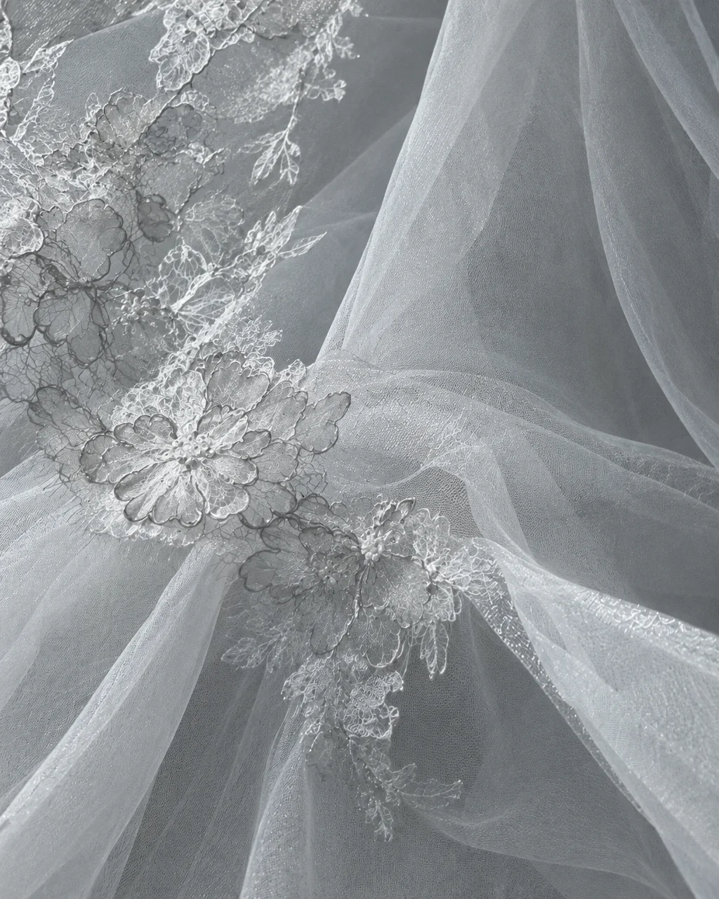 Intricate floral lace embroidery layered over draped sheer white tulle fabric.