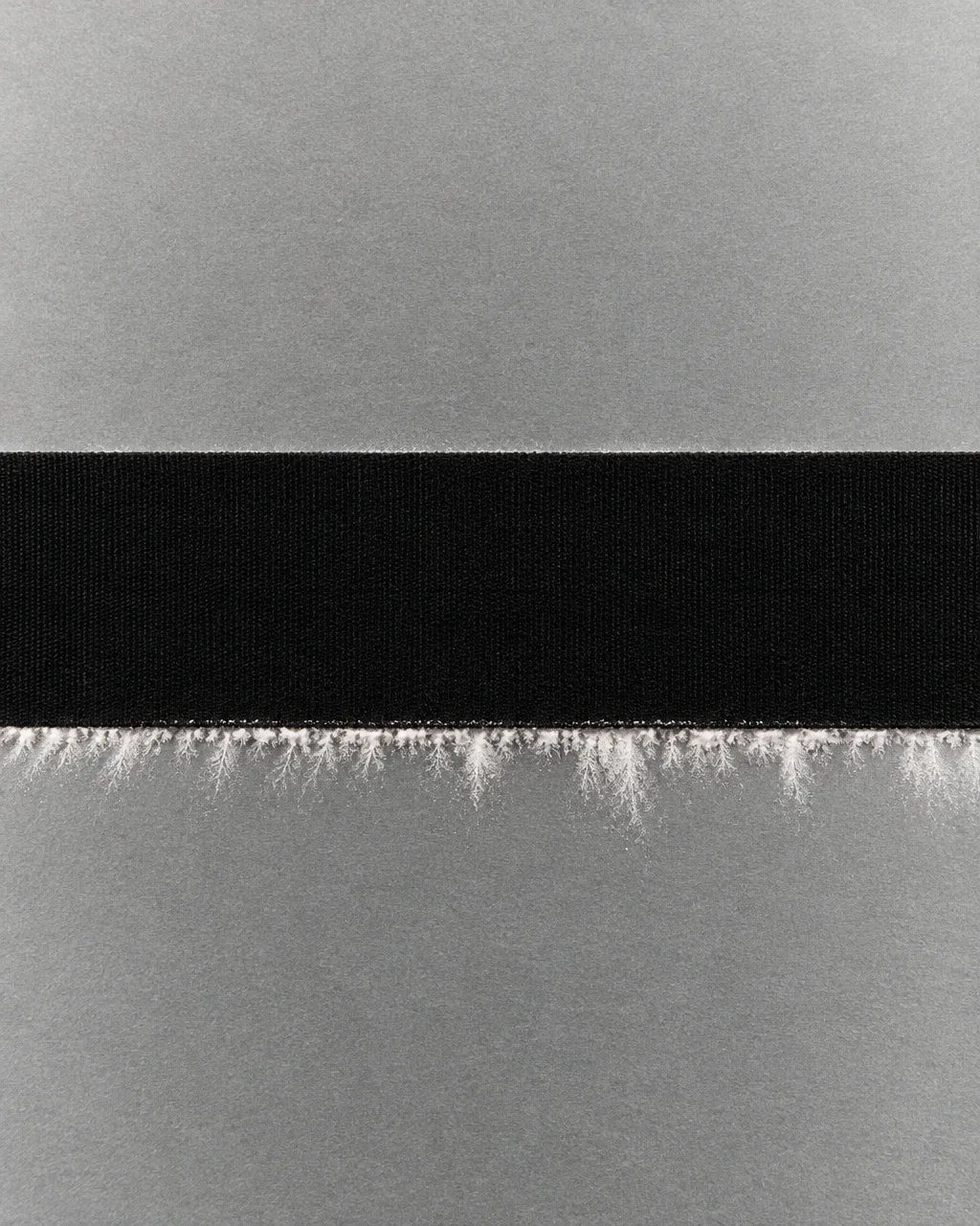 A horizontal black textured tape strip centered on grey cardstock, edged with delicate white dendritic frost patterns.