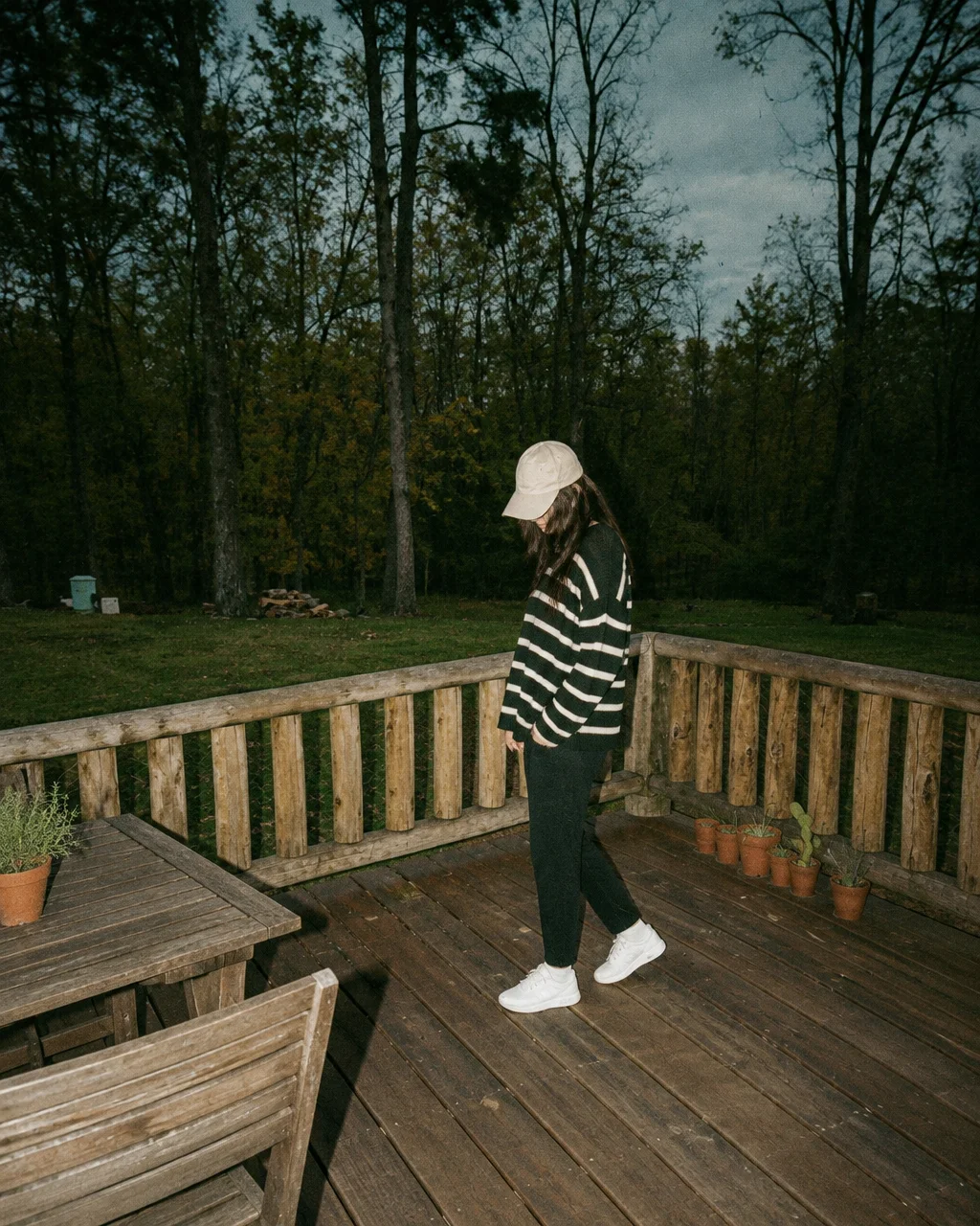 A person in a striped sweater and baseball cap standing on a rustic wooden deck against a dark woodland backdrop.