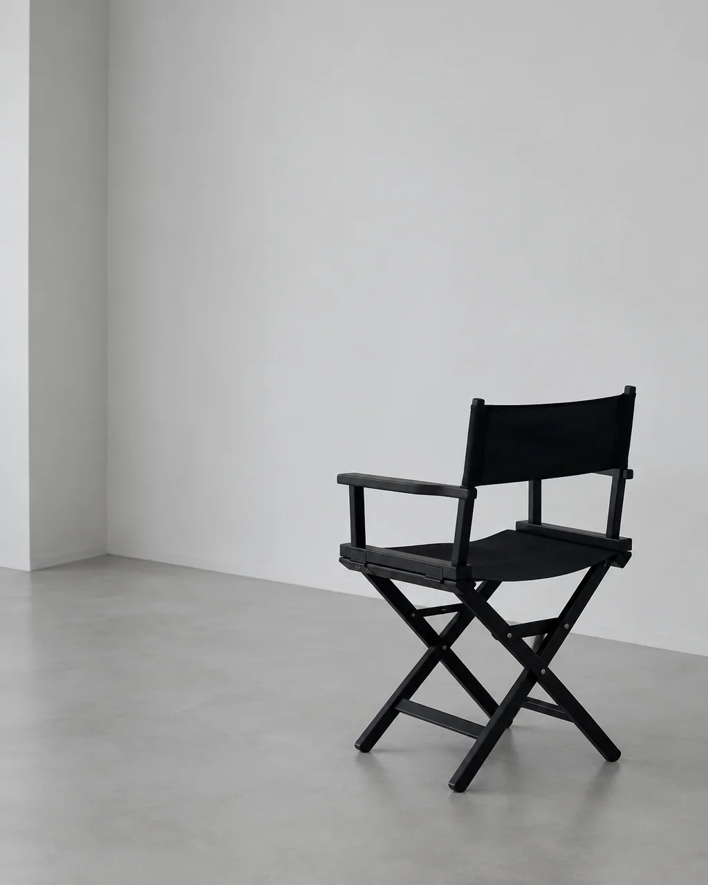 A black director's folding chair sits alone on a polished concrete floor against empty white studio walls.