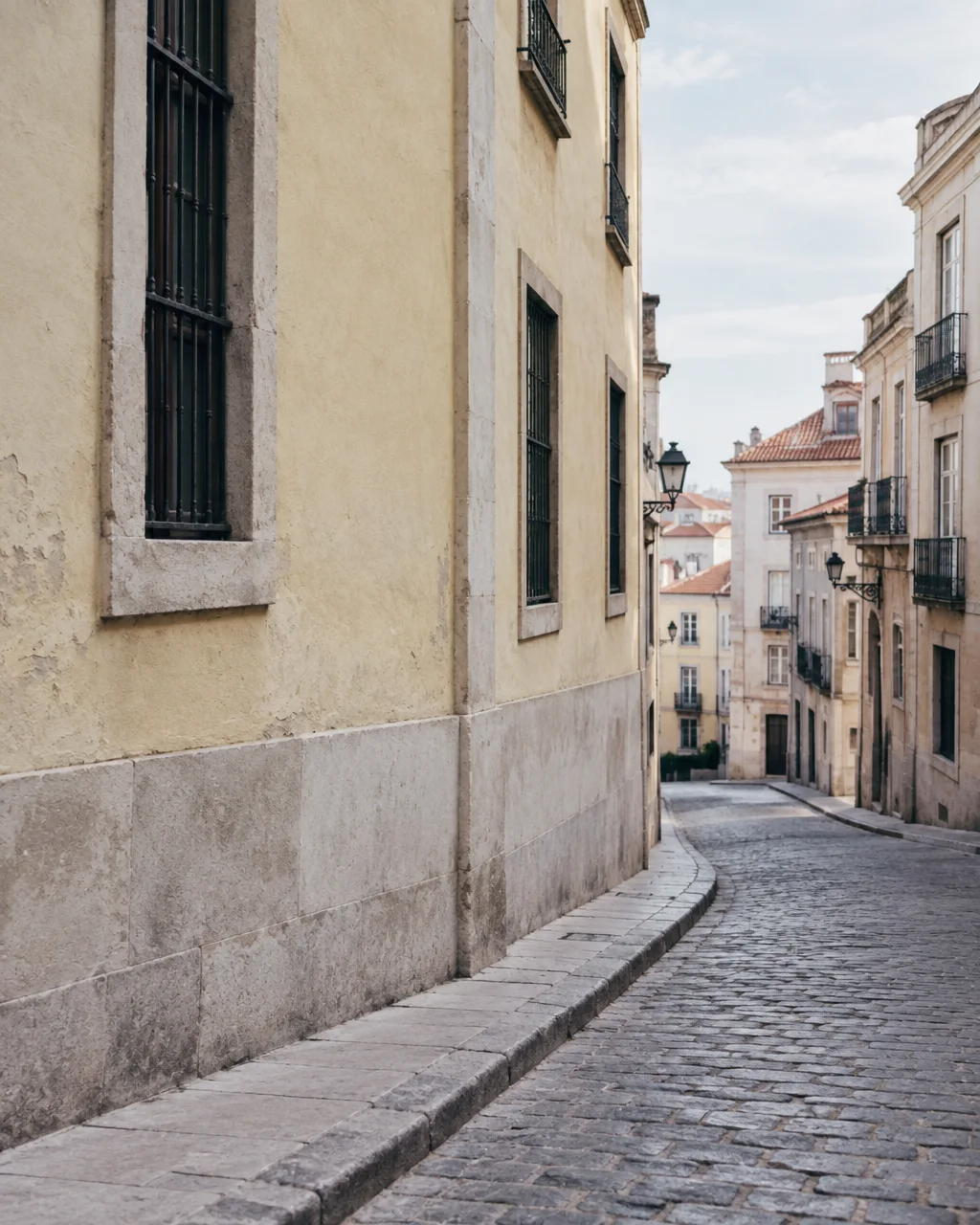 A quiet, curving cobblestone street lined with pale yellow stucco facades and historic architecture in soft daylight.