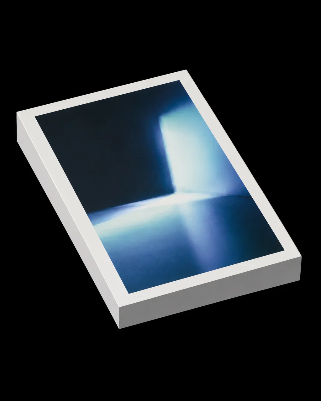 A white hardcover book angled over a pure black background, featuring an abstract cover print of glowing blue light spilling into a dark room.