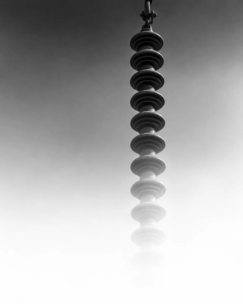 A vertical power line insulator string fades downward into bright white mist in high-contrast black and white.